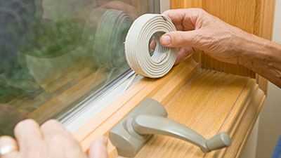 Hands are shown applying weather stripping to a window