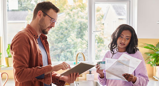 thumbnailfor Homeowners standing in their kitchen looking at papers and a computer tablet