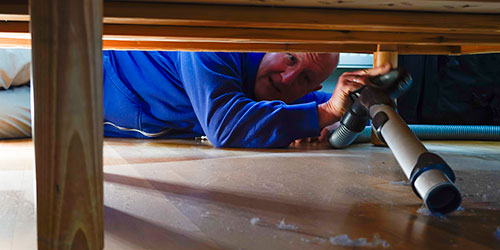 man vacuums dust under chair