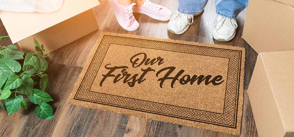 Couple standing in front of first home welcome mat