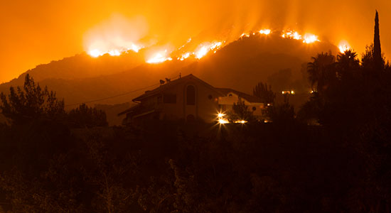 A wildfire burns on the hills above a home