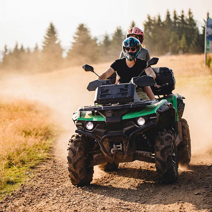 Two people riding an atv on a dirt road