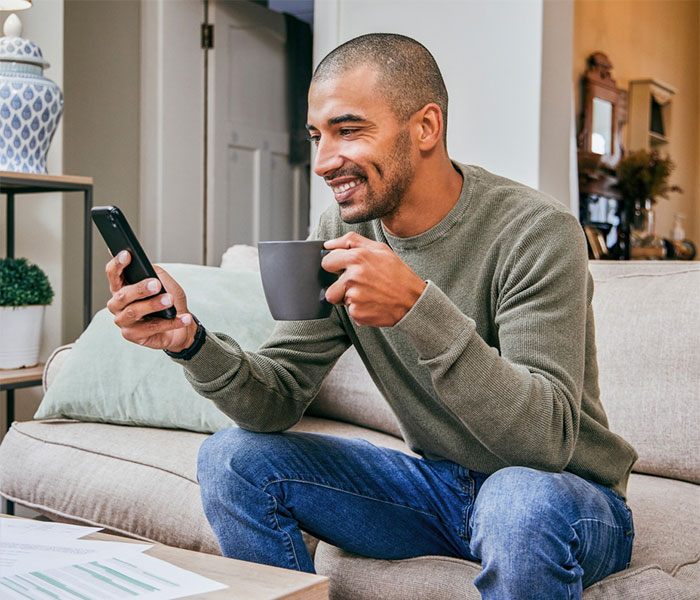 A man reads text messages on his phone while drinking coffee at home