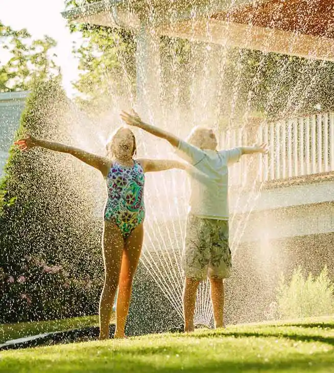 Young girl and boy playing in sprinkler