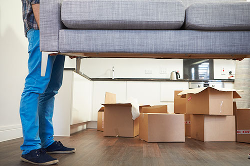 Man moving couch to new home from old home around cardboard boxes thumbnail