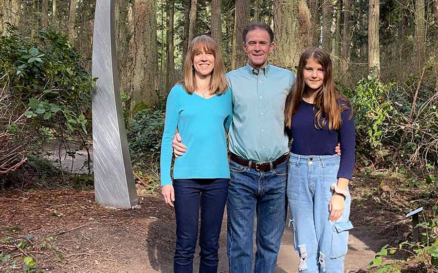 Family of three posing for picture with forest backdrop